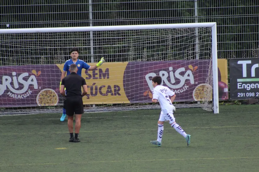 Guarda-redes a levantar o braço para orientar a defesa enquanto um adversário corre para a área, em jogo.