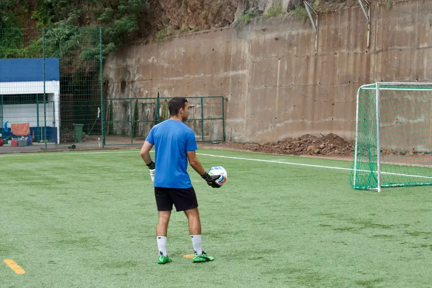 Treinador com a bola nas mãos a preparar o exercício seguinte, junto a uma baliza reduzida.