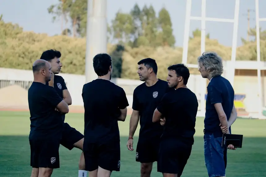Equipa técnica reunida em círculo no relvado, antes do treino.